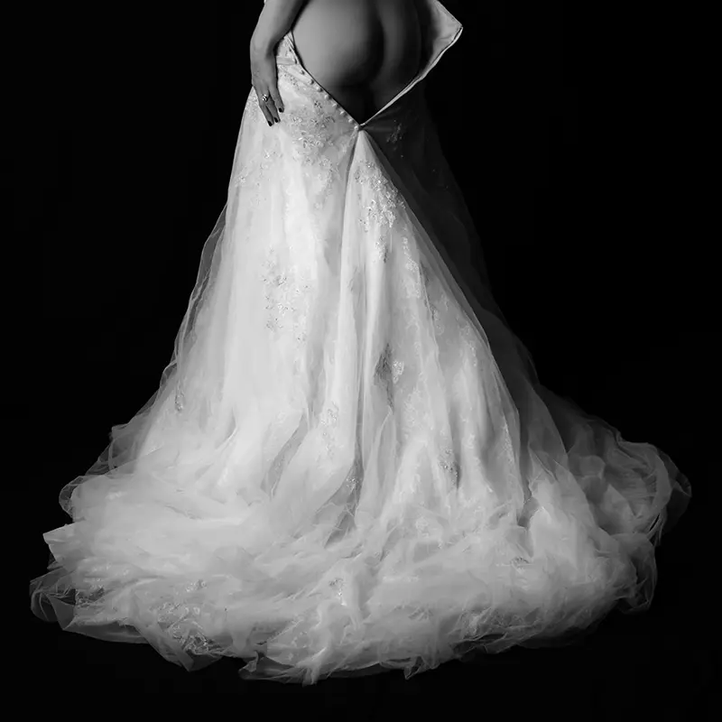 Black and white image of the back of a bridal gown just showing the bare bottom of the model wearing it