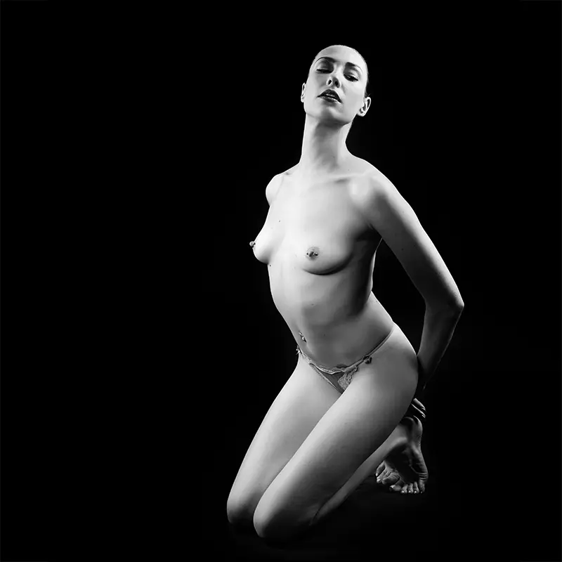 Black and white image of a naked woman kneeling in a submissive pose